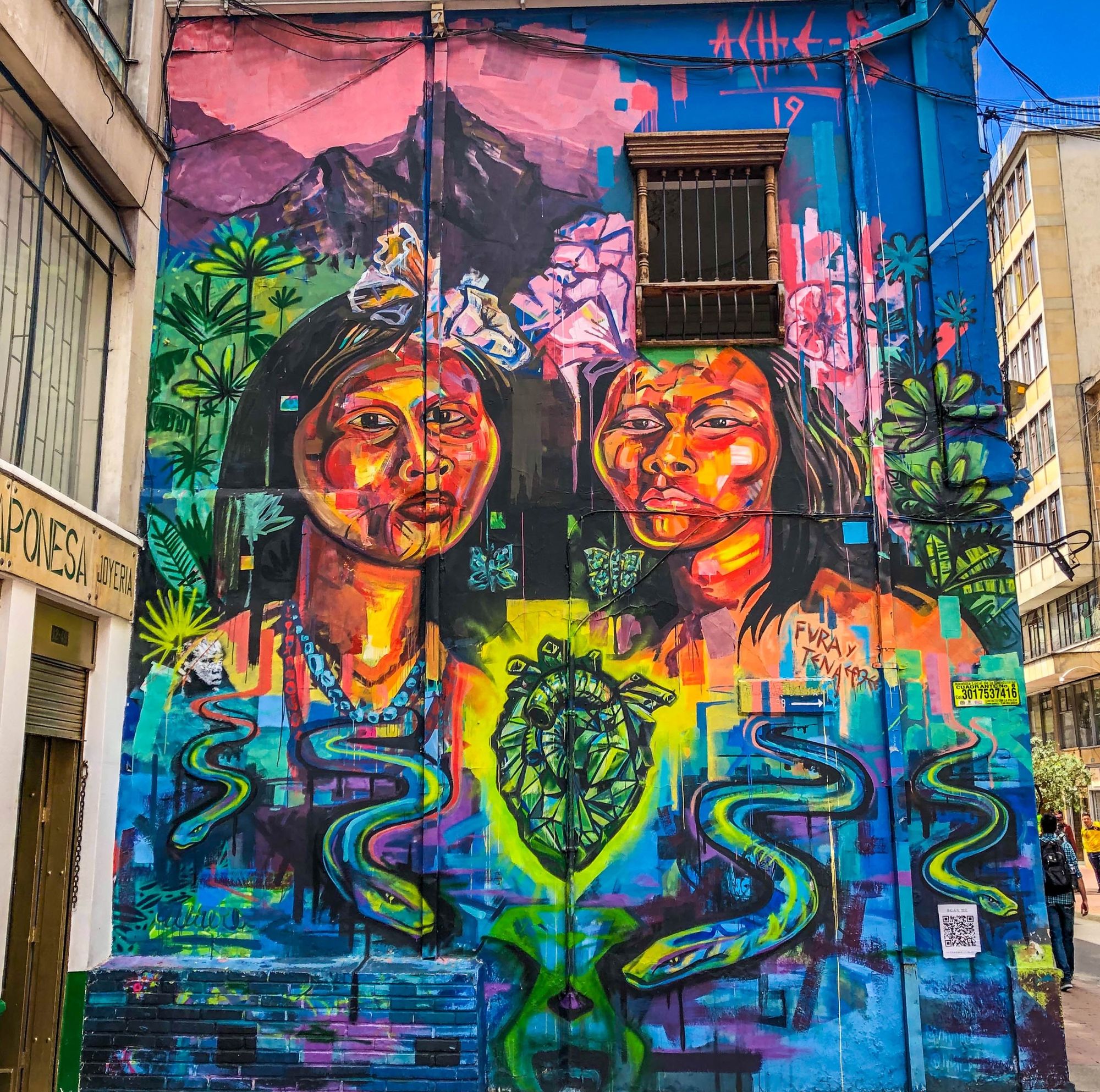 A colorful painted wall with two indigenous people, plants, flowers, a big heart and snakes